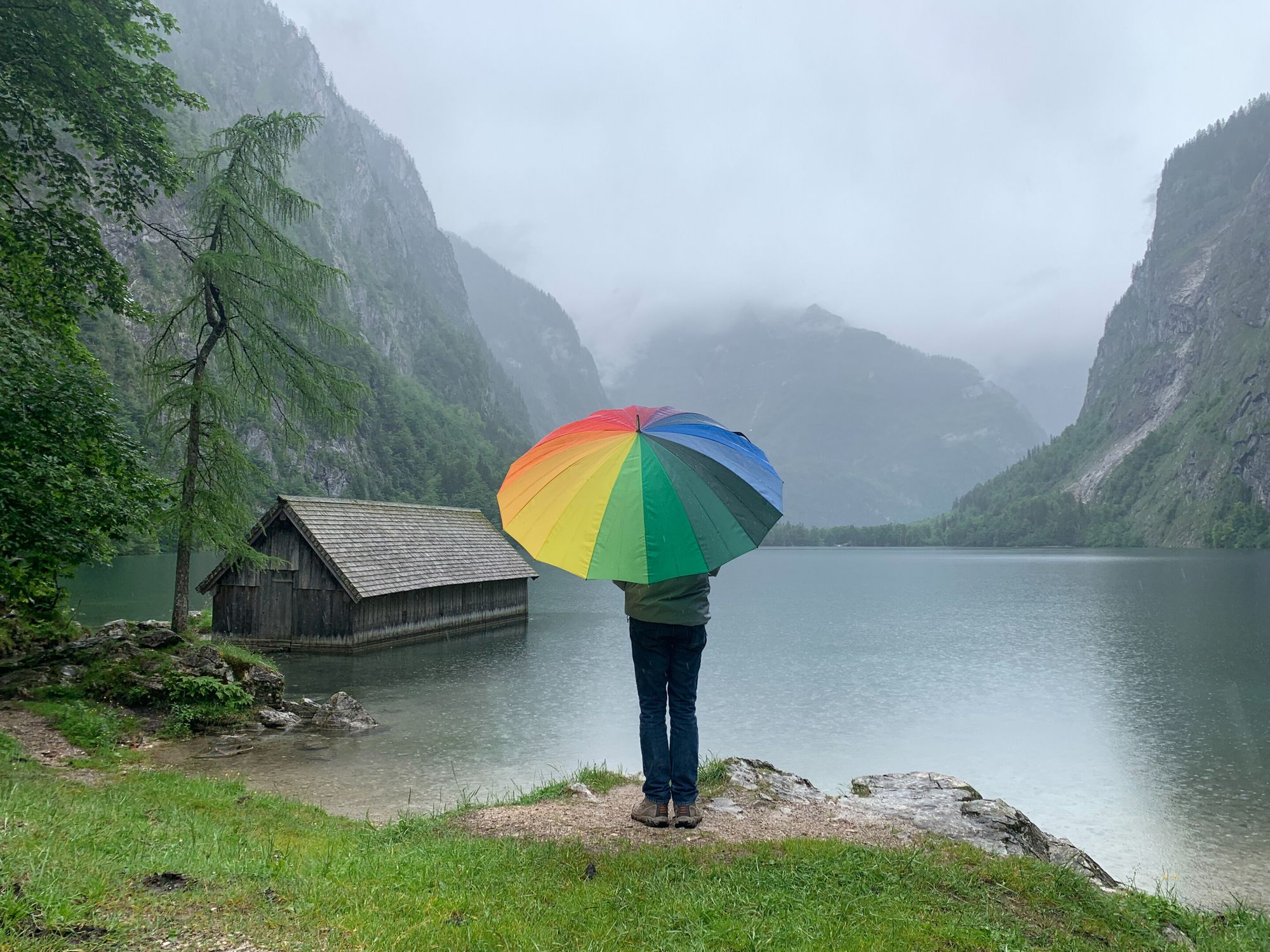Ryan facing a lake with a rainbow umbrella covering is head.