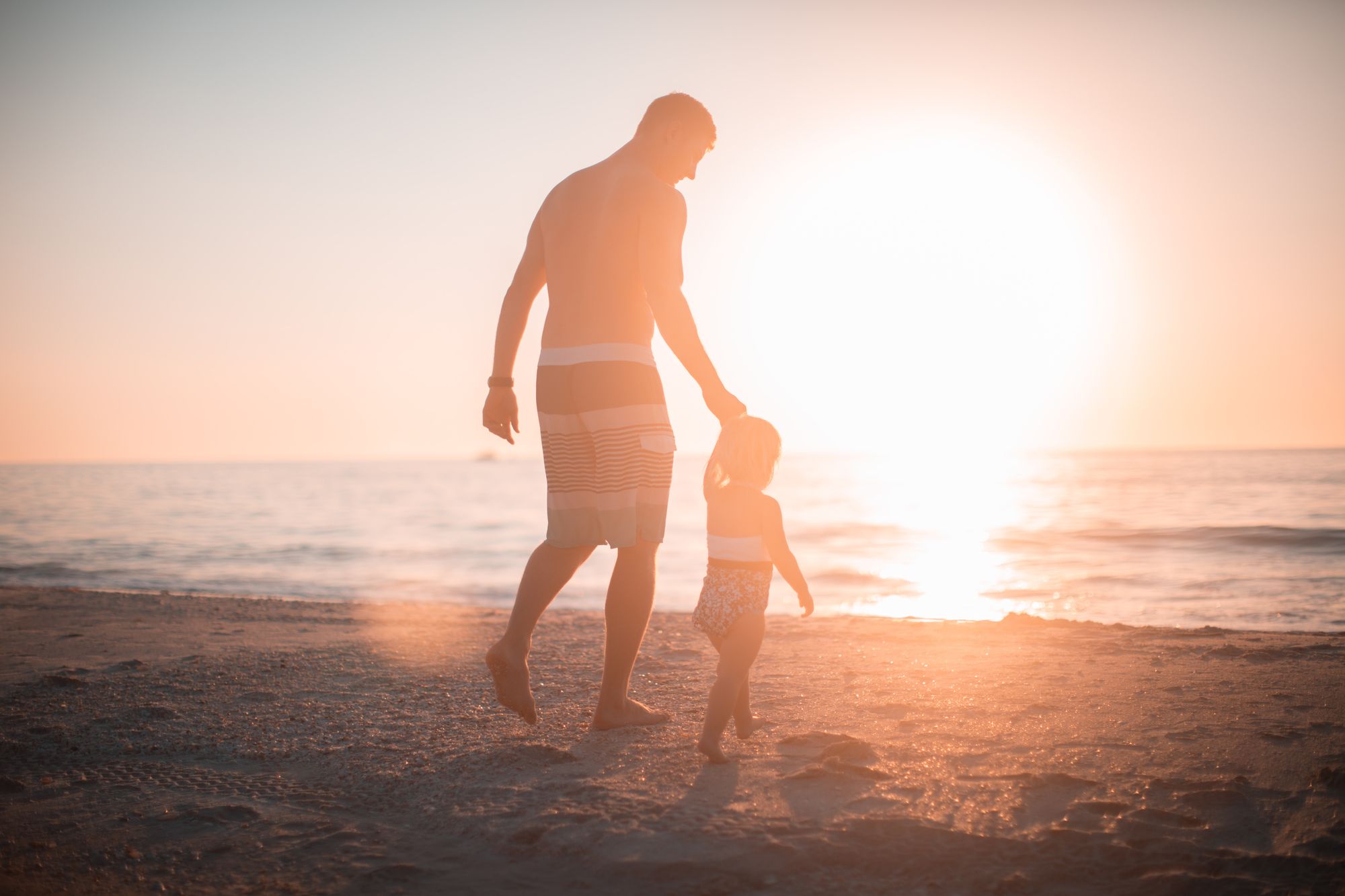 Parent and child walking on the beach while holding hands.