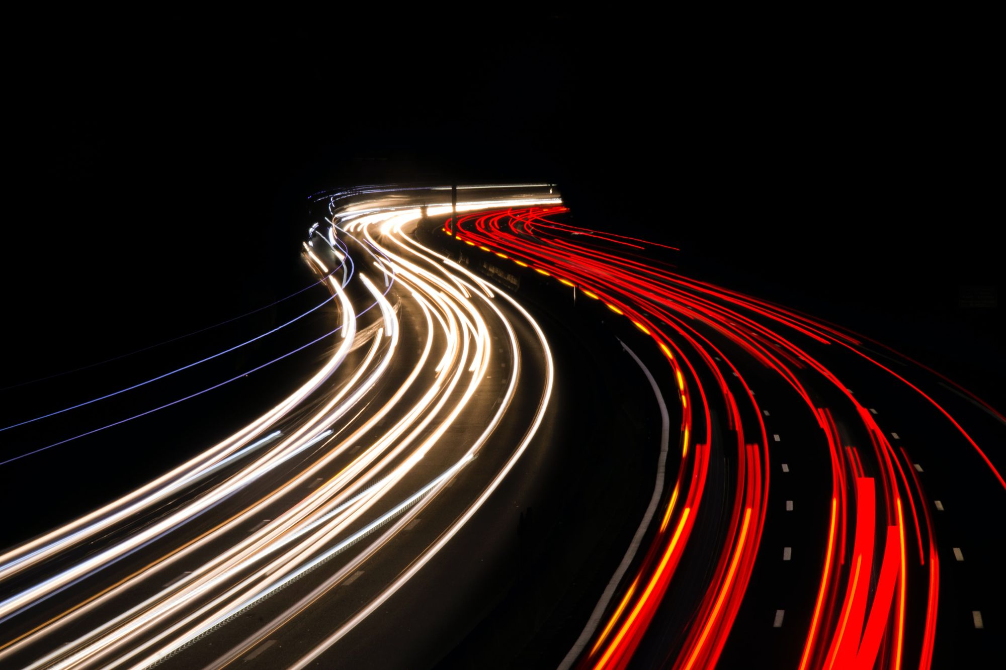 Arial view of a road with streaks of headlights and tail lights.