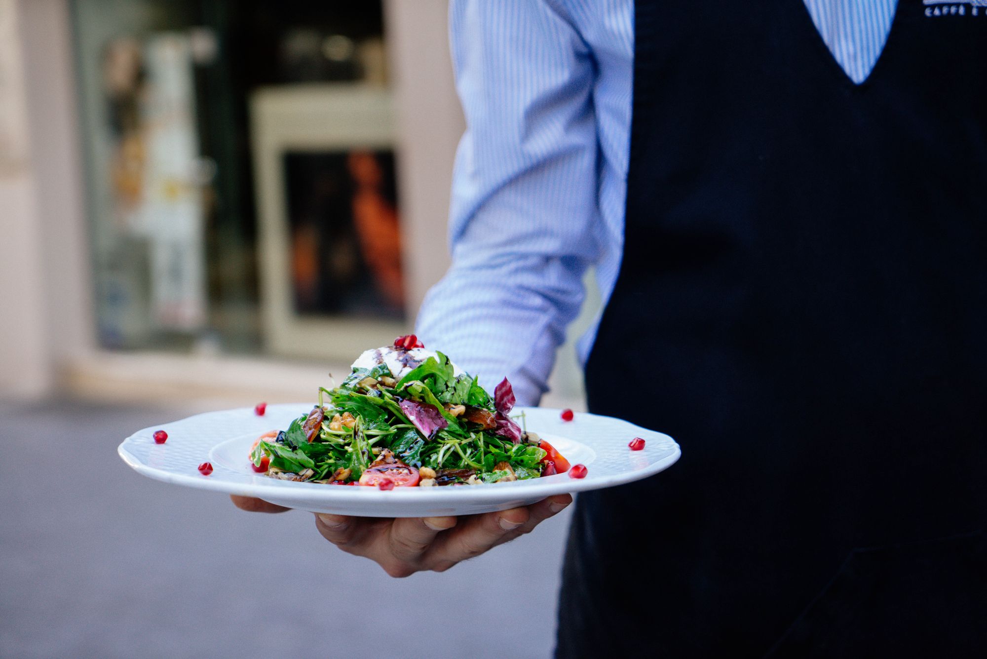 Server holding a beautifully decorated plate with salad.