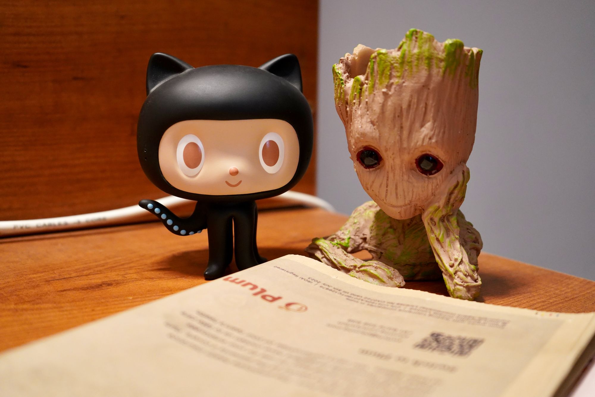 Octocat and a baby Groot looking over a newspaper.
