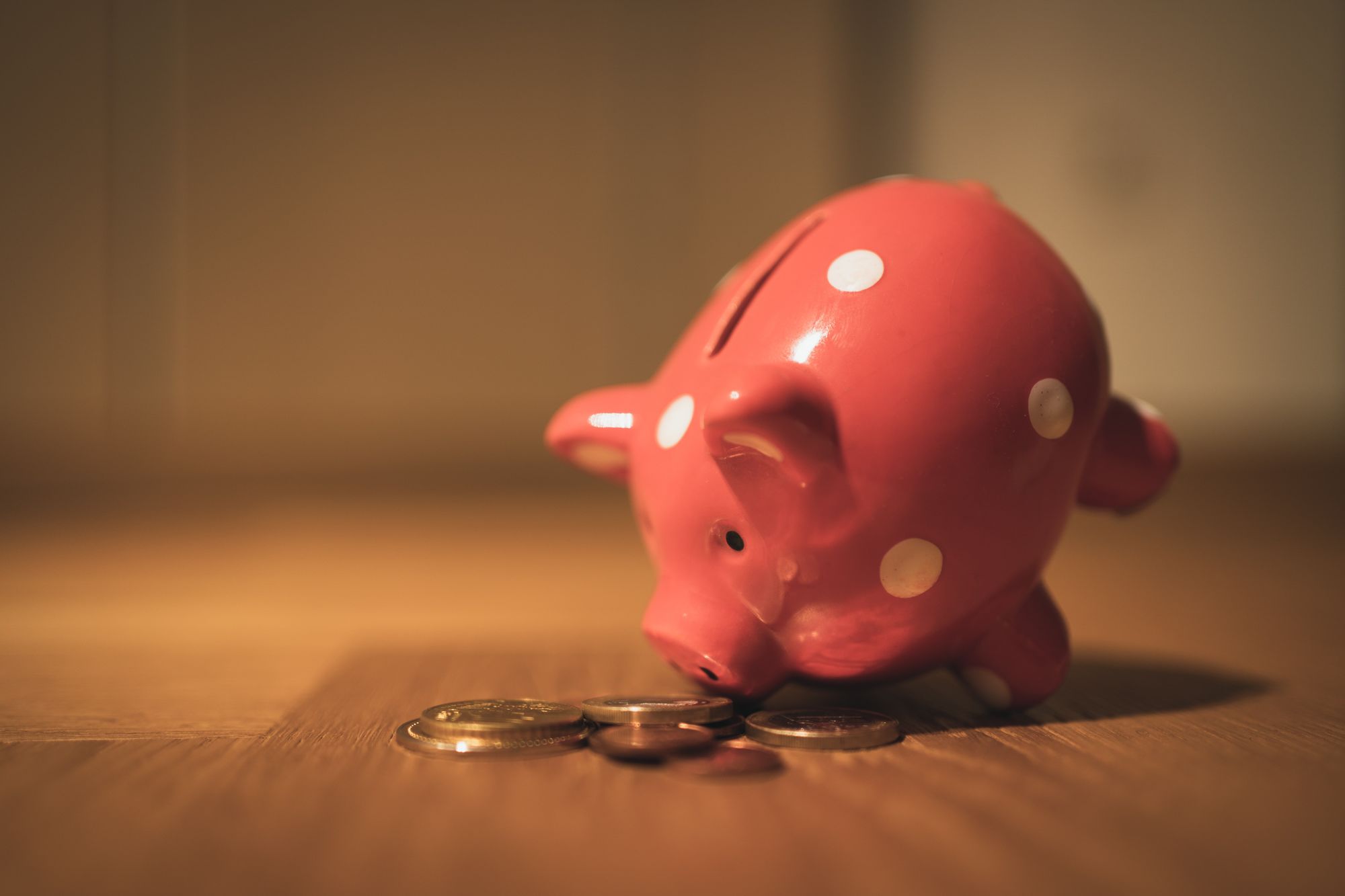 Piggybank leaning on its nose on top of a pile of coins.