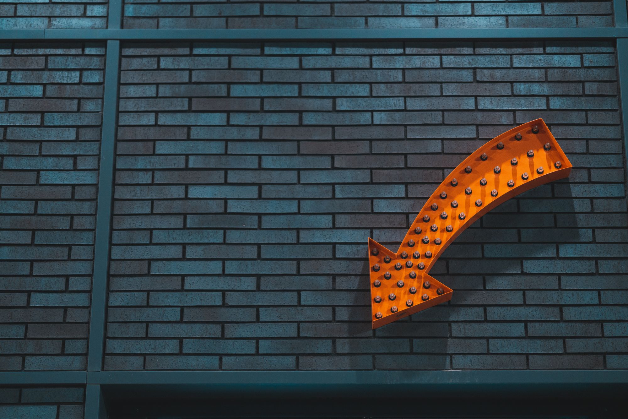 Orange arrow, on a brick wall, pointing down.