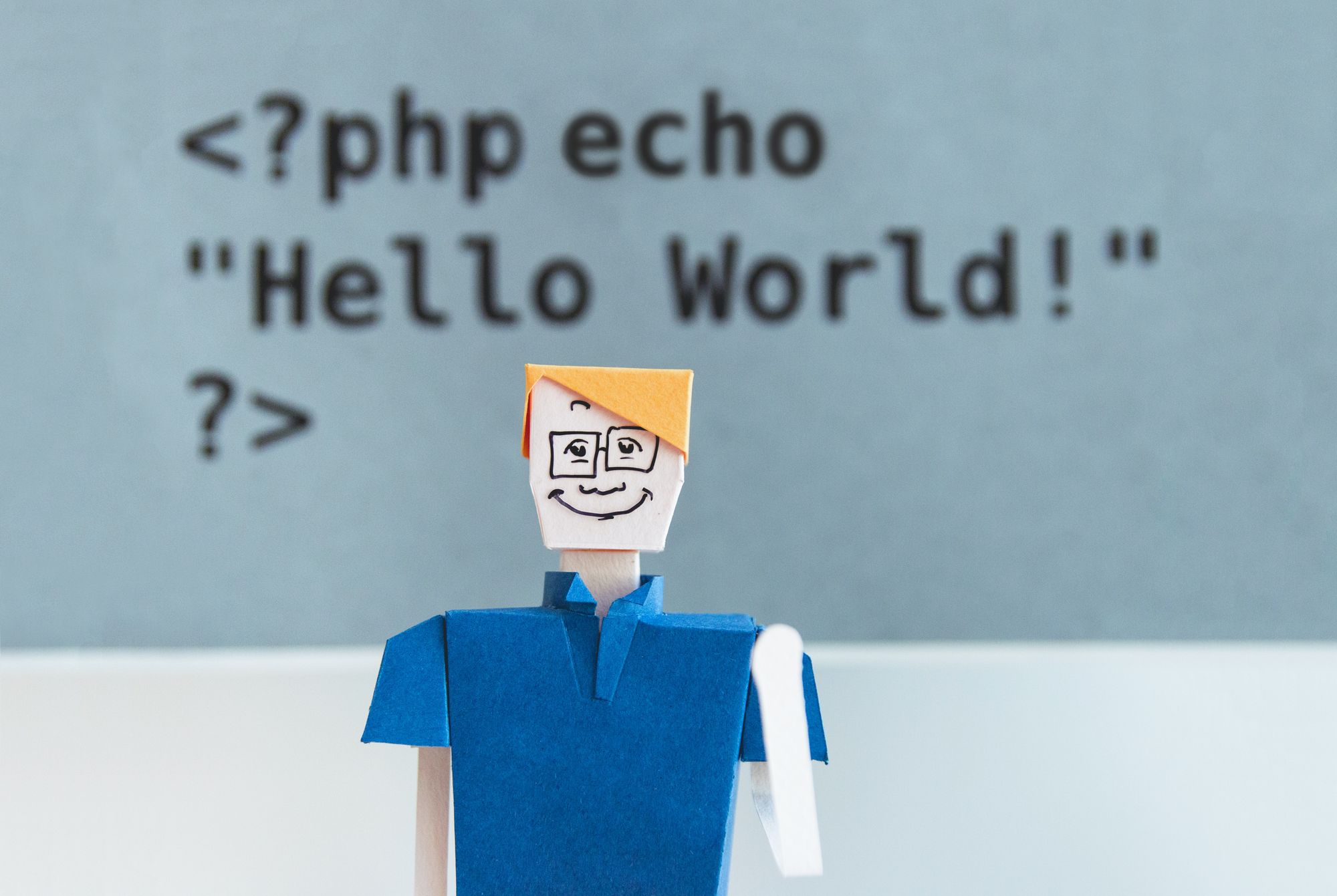 Paper figure in front of a board of PHP code.