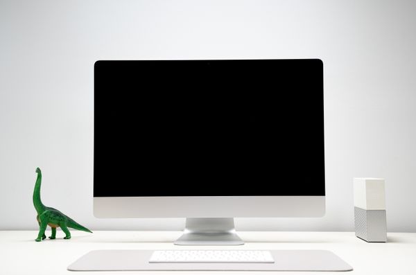 White table with white computer appliances and a green dinosaur.